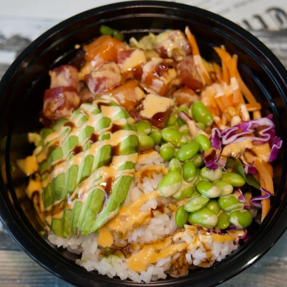 A colorful poke bowl with tuna, avocado, edamame, carrots, and red cabbage over rice.