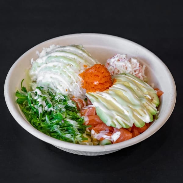A colorful poke bowl with salmon, avocado, seaweed salad, rice, and roe in a white bowl.