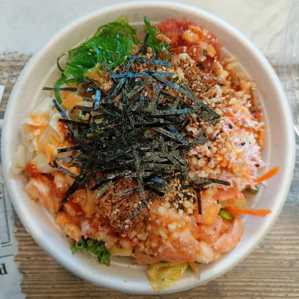 A colorful poke bowl with salmon, tuna, seaweed, and shredded nori on a wooden table.
