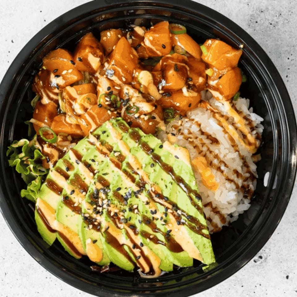 A poke bowl with salmon, avocado, rice, and greens, drizzled with sauces and sesame seeds.