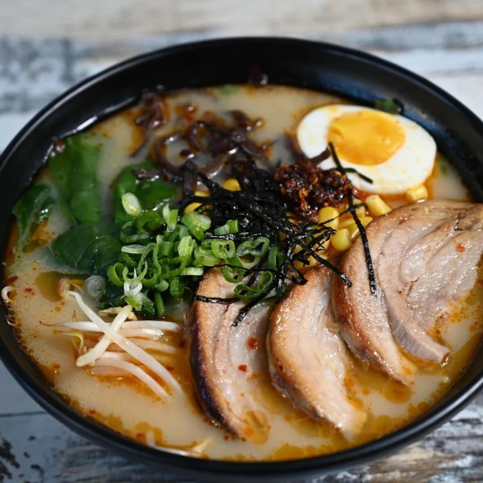 A close-up of a bowl of ramen with pork, egg, corn, seaweed, and green onions.