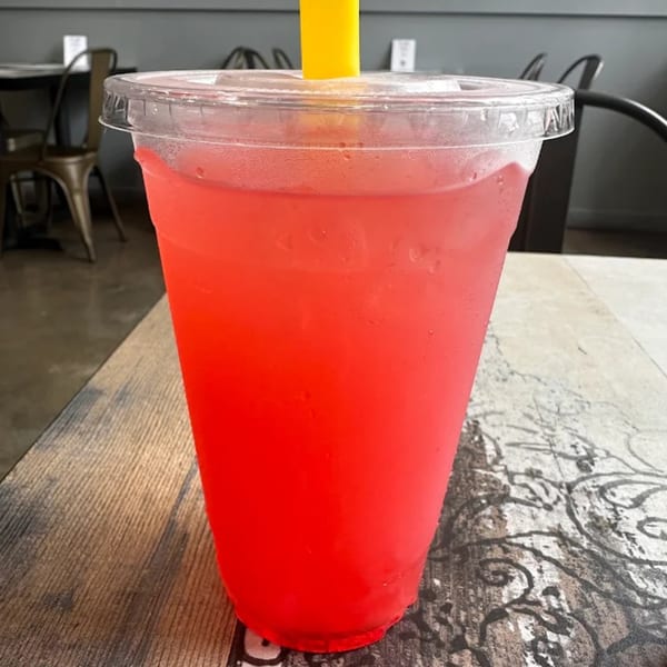 A vibrant red drink in a clear plastic cup with a yellow straw sits on a patterned wooden table.