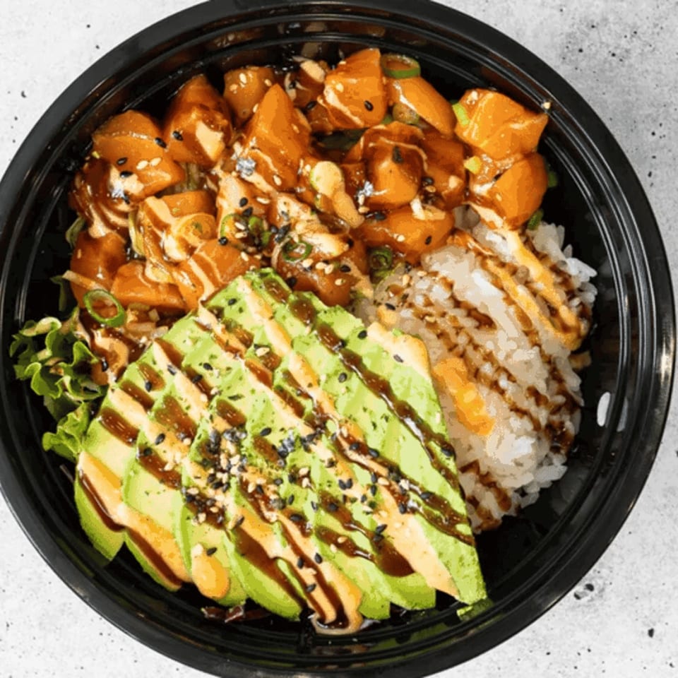 A poke bowl with salmon, avocado, rice, and greens, drizzled with sauces and sesame seeds.