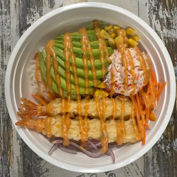 A poke bowl with tempura shrimp, avocado, corn, crab salad, carrots, and red onions.