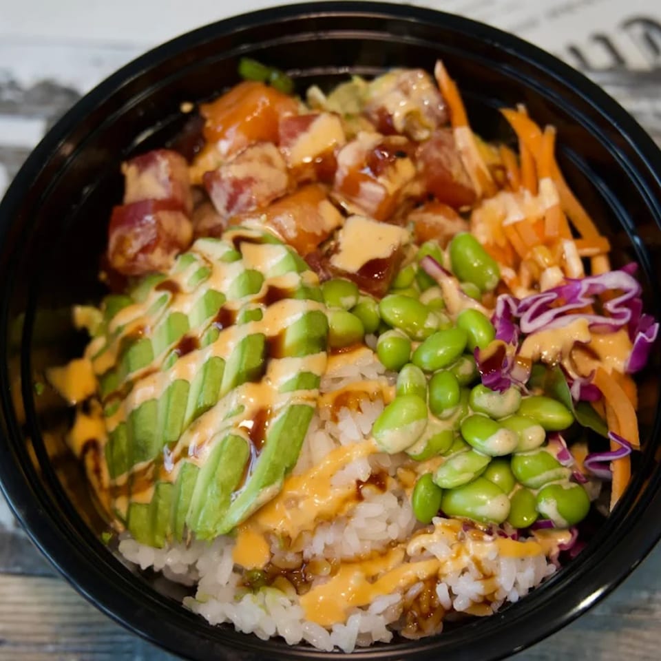 A colorful poke bowl with tuna, avocado, edamame, carrots, and purple cabbage over rice.